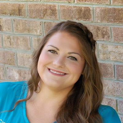 Financial Coordinator Carrie Fuller Smiling In Front Of Brick Wall