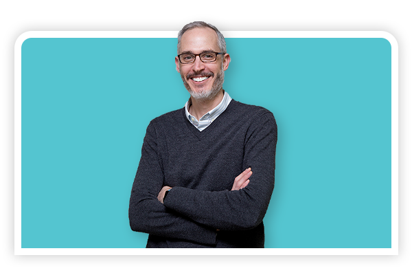 Orthodontist Gibson McCall Smilign In Front Of Blue Background