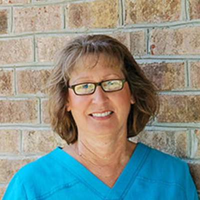 Orthodontic Assistant Susan Woolard Smiling In Front Of Brick Wall